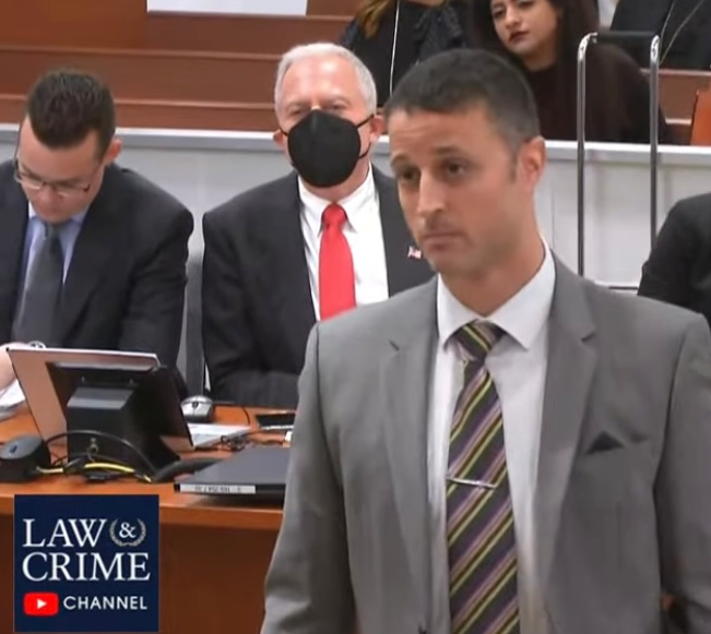 A man in a suit and tie stands in front of a law & crime channel sign