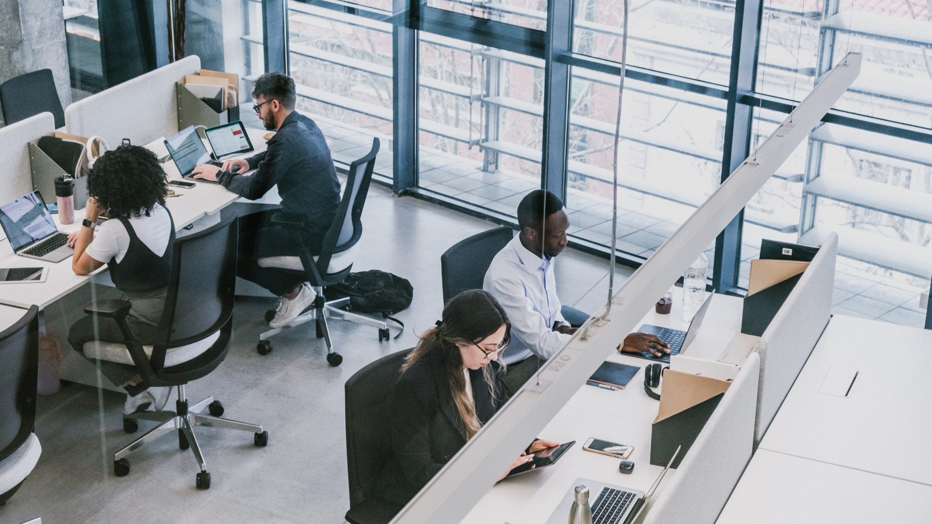 A group of people are sitting at desks in an office using laptops.