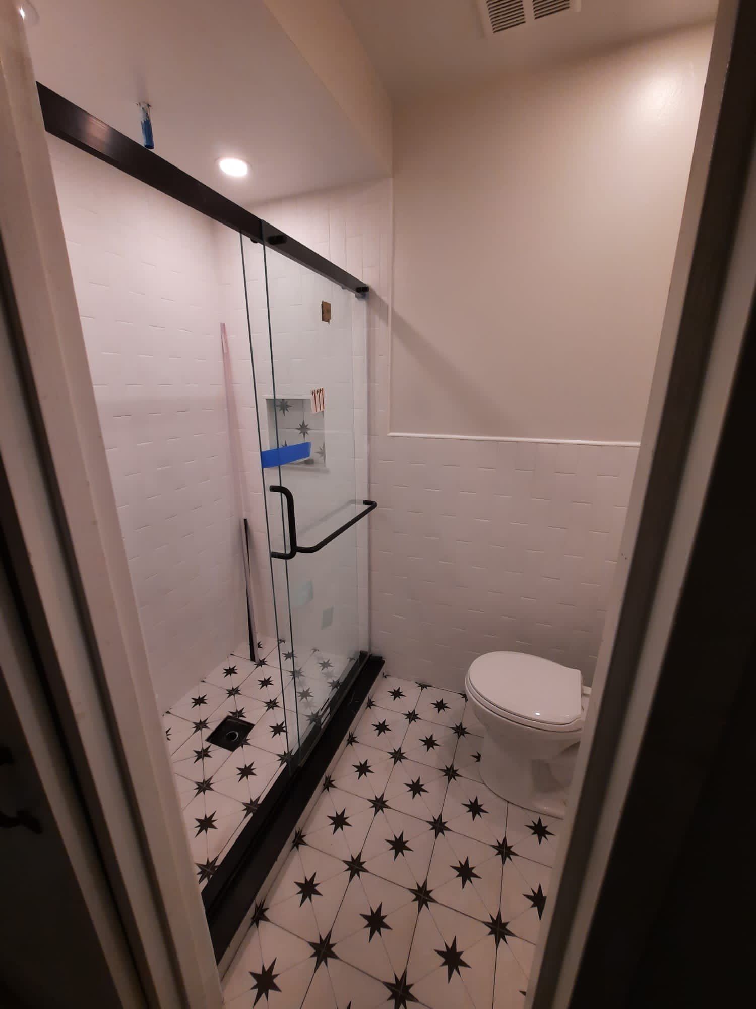 Small bathroom with shower and toilet, black and white star patterned floor, glass shower door.