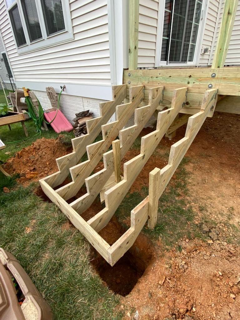 Wooden staircase construction attached to a deck, set in a grassy yard.