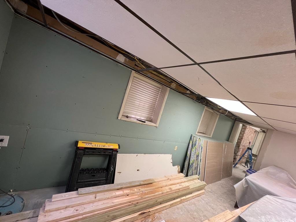 Room under renovation, showing exposed ceiling, green wall, window, and construction materials.