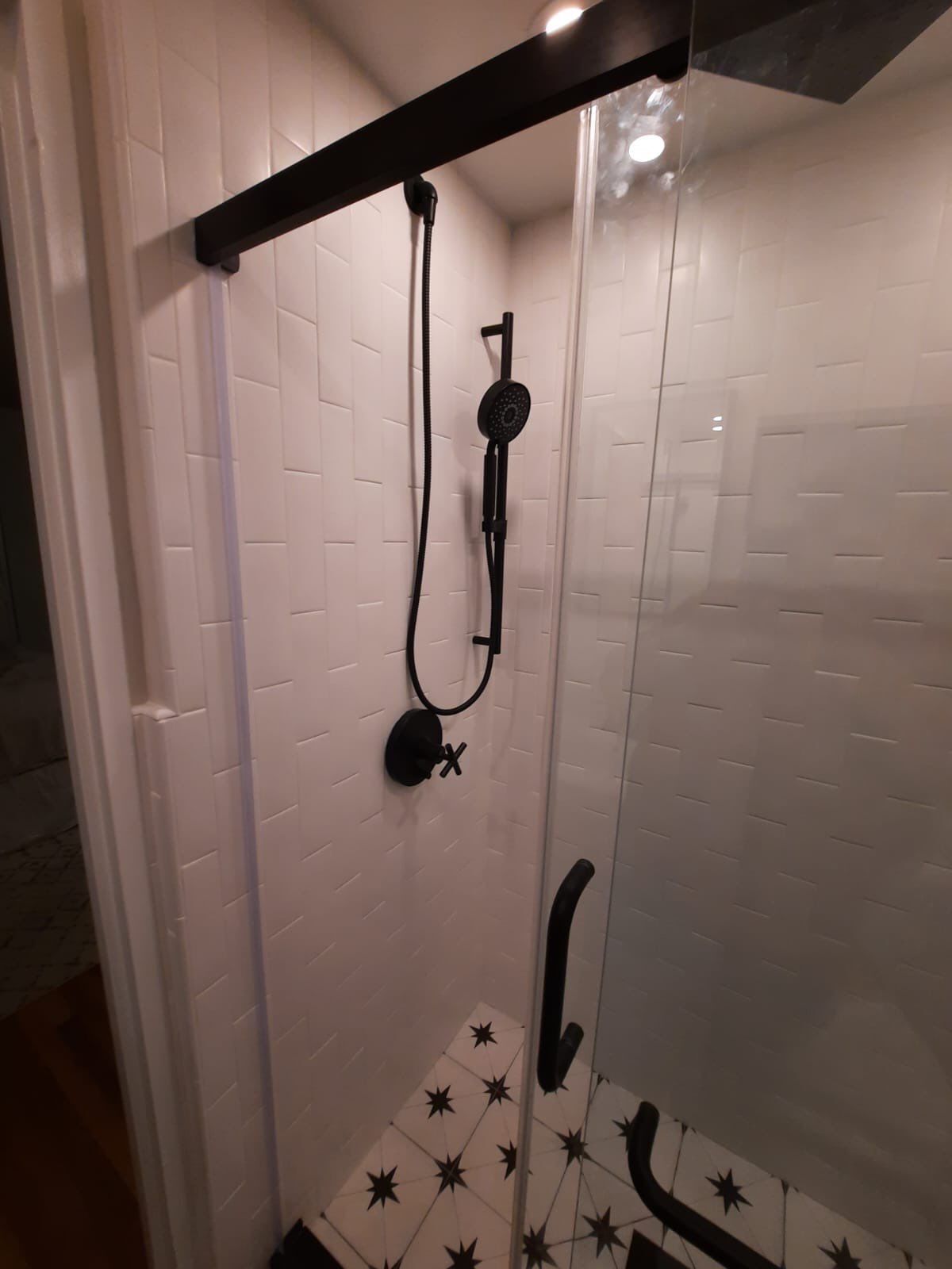 Black shower fixture in a white tiled shower with a glass door.