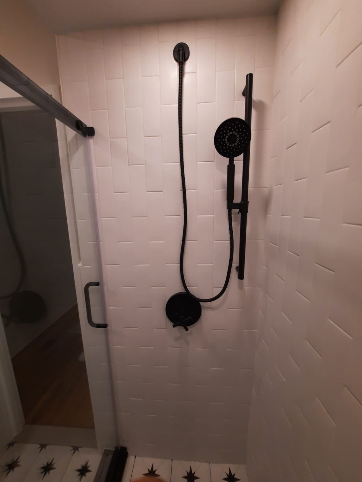 Black shower fixtures on white tiled wall. Sliding glass door visible to the left.