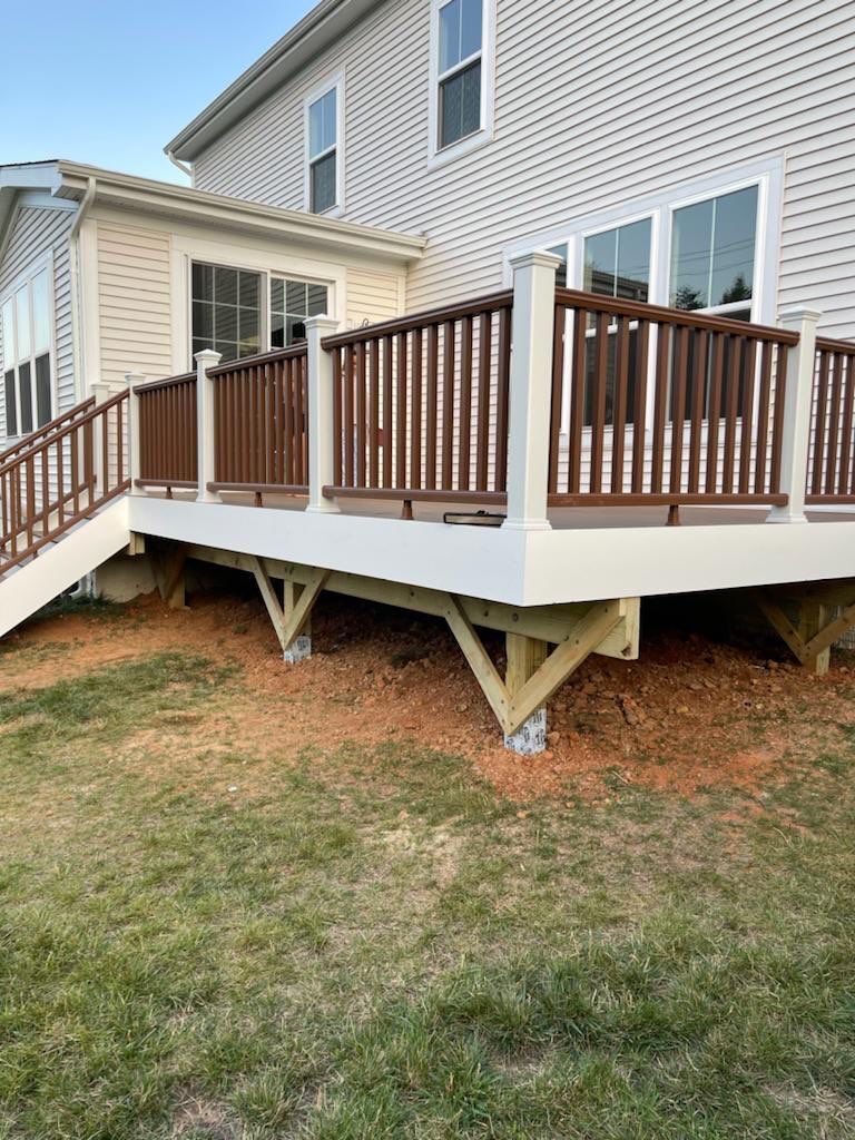 A newly built deck attached to a house with brown railing and white support beams on a grassy lawn.
