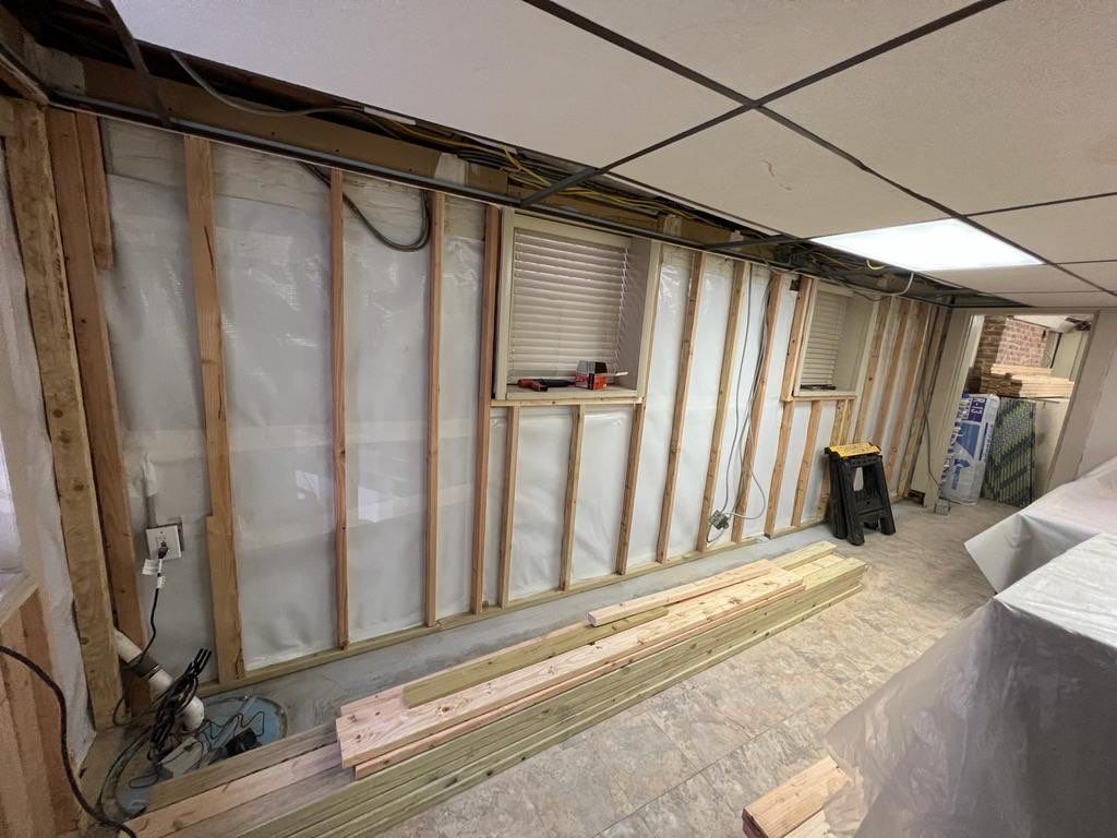 Basement wall construction: wood studs, insulation, vapor barrier, windows. Lumber on floor.
