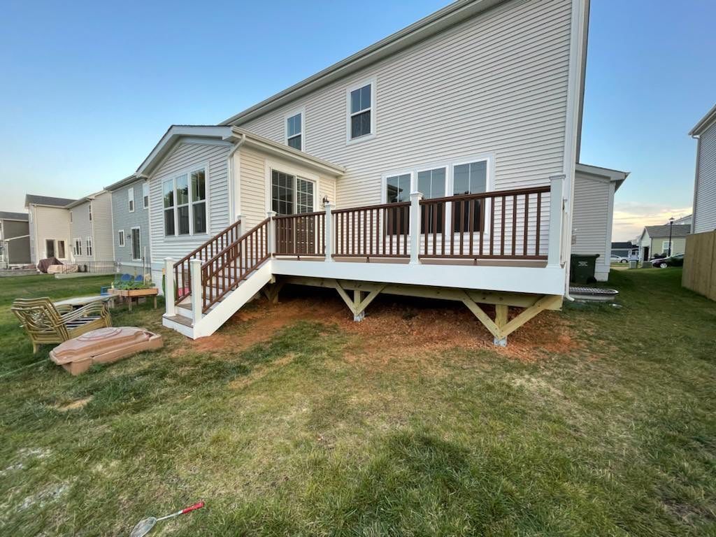 Back view of a two-story house with a wooden deck; brown deck and railing, white house, and green grass.