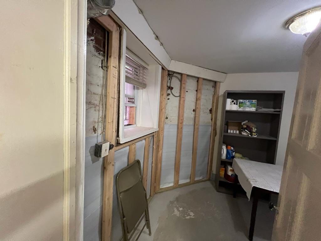 Basement room under renovation with exposed studs, a window, and a folding chair.