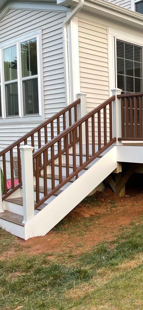 Exterior stairs with brown railing and white trim leading up to a house.