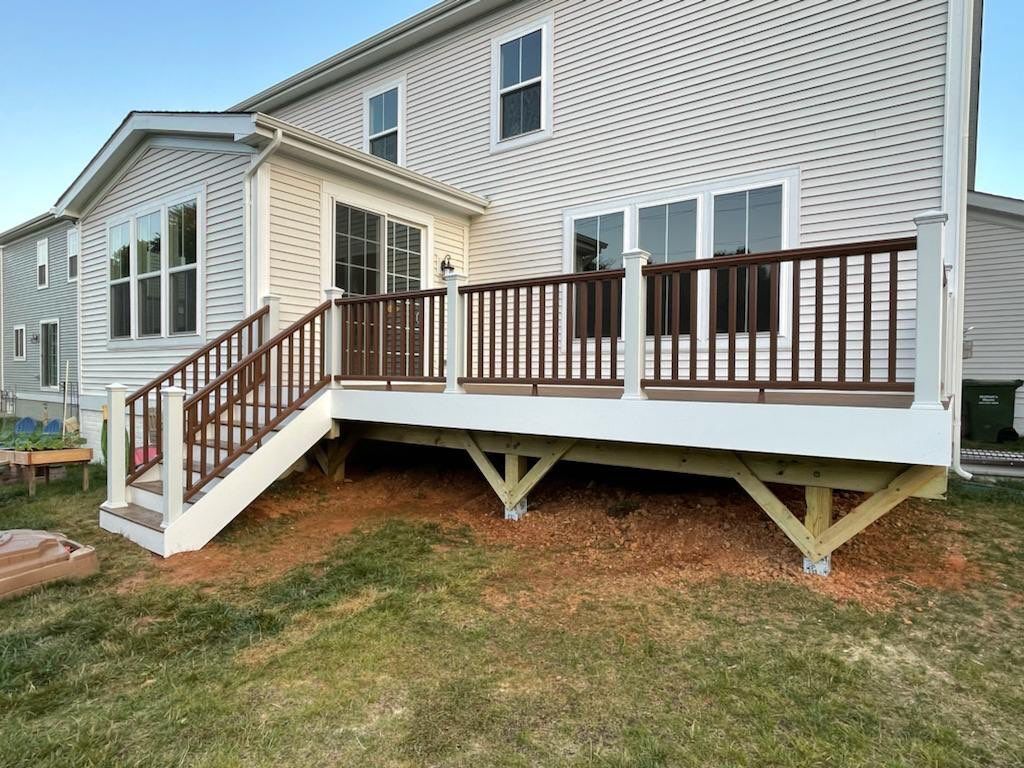 A newly built deck attached to a two-story house, with brown railings and white trim.