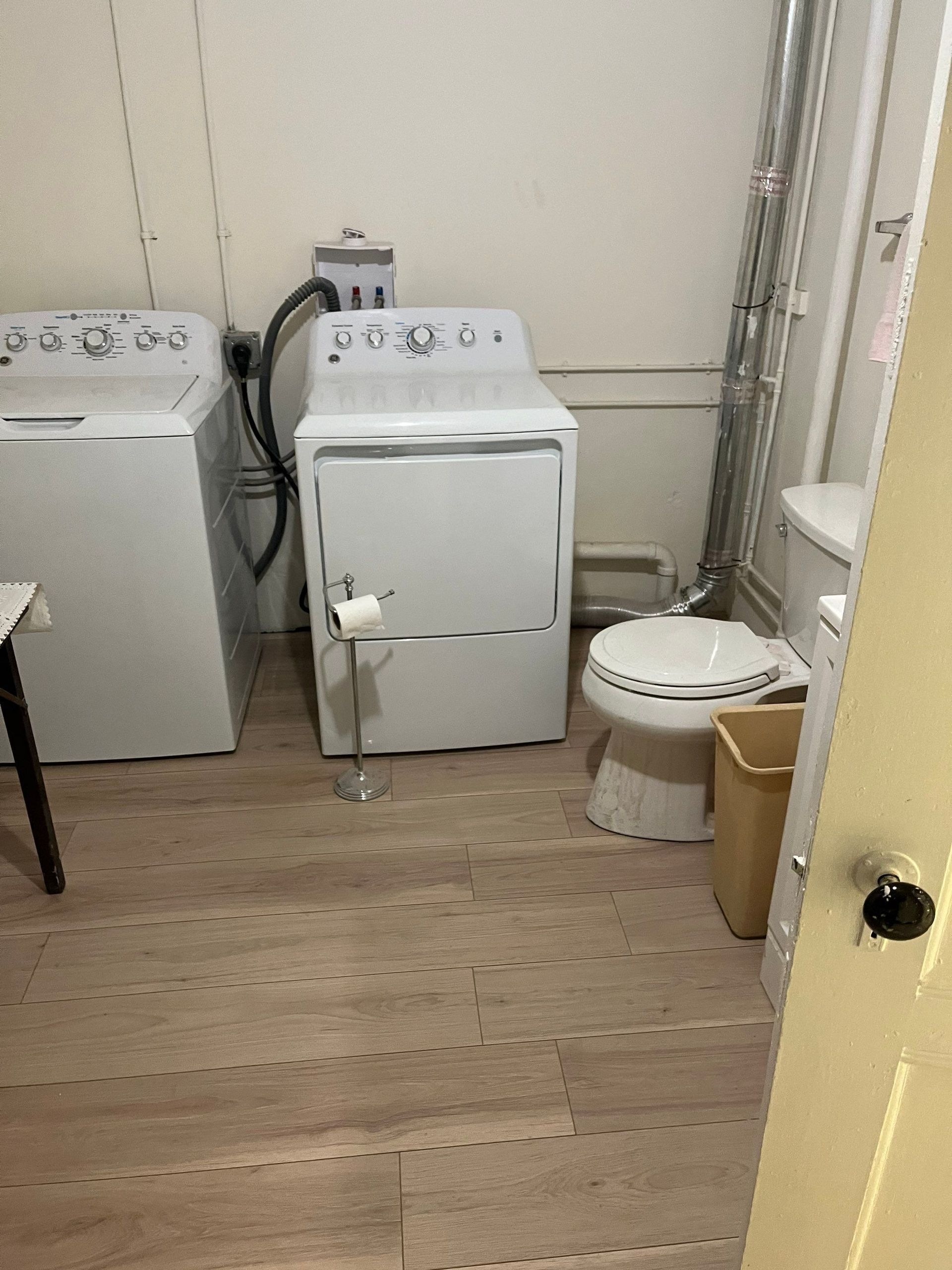 Laundry room with washing machine, dryer, and toilet. Light-colored flooring and walls.