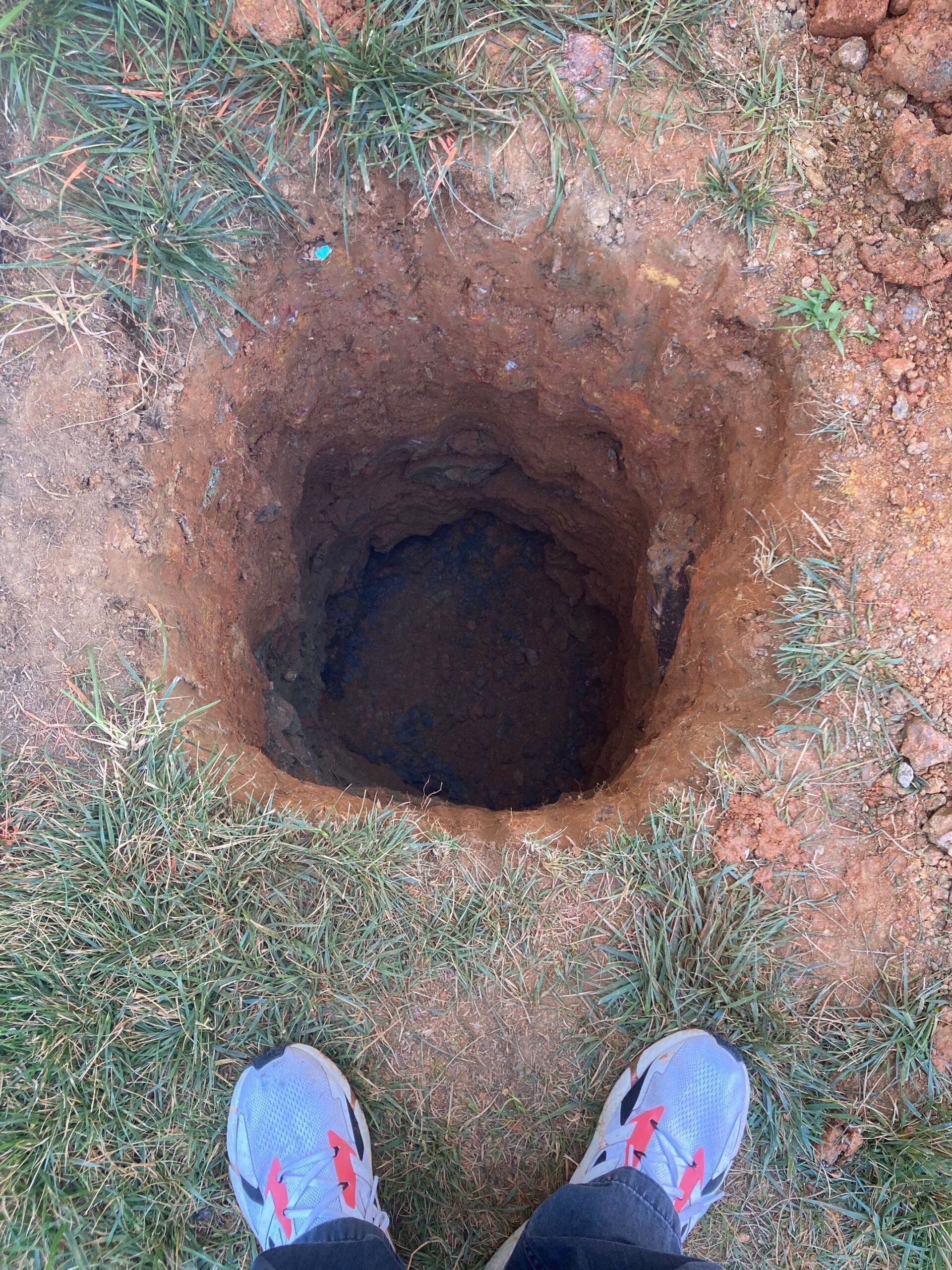 A deep, round hole in the ground with a person's feet visible at the top.
