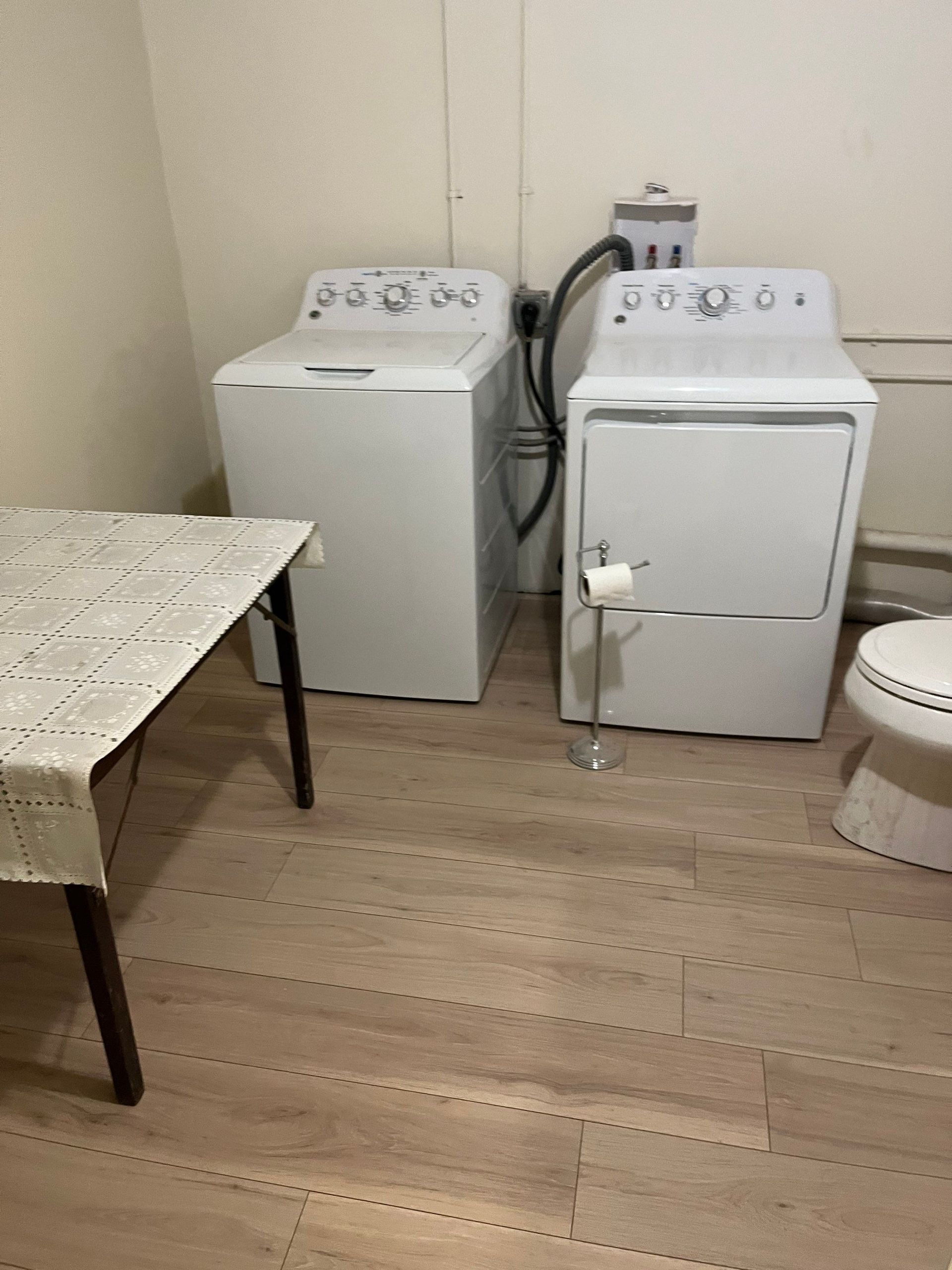 A white washing machine and dryer in a laundry room, next to a table and toilet.