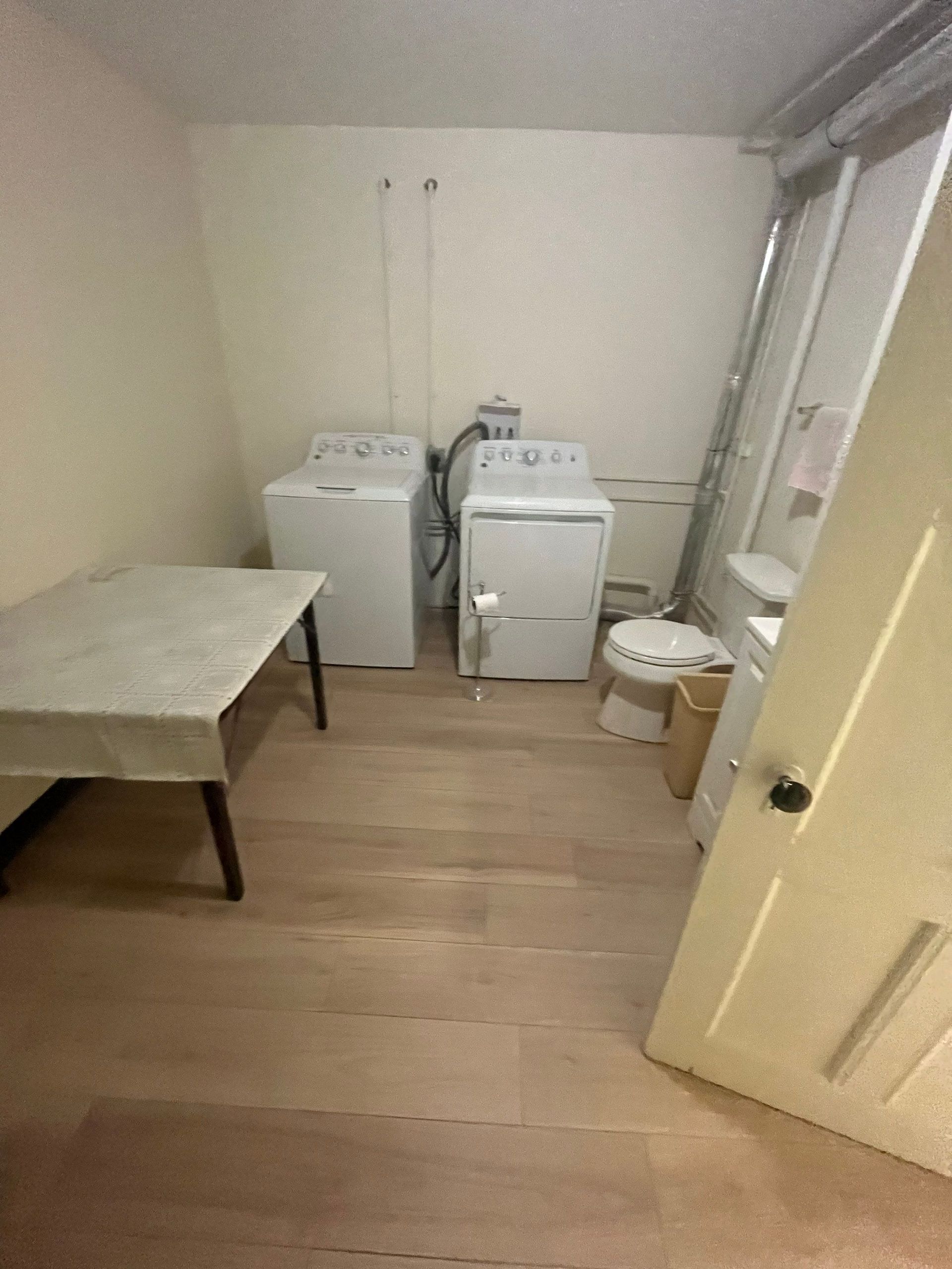 Laundry room with washing machine, dryer, table, and door on light wood floor.
