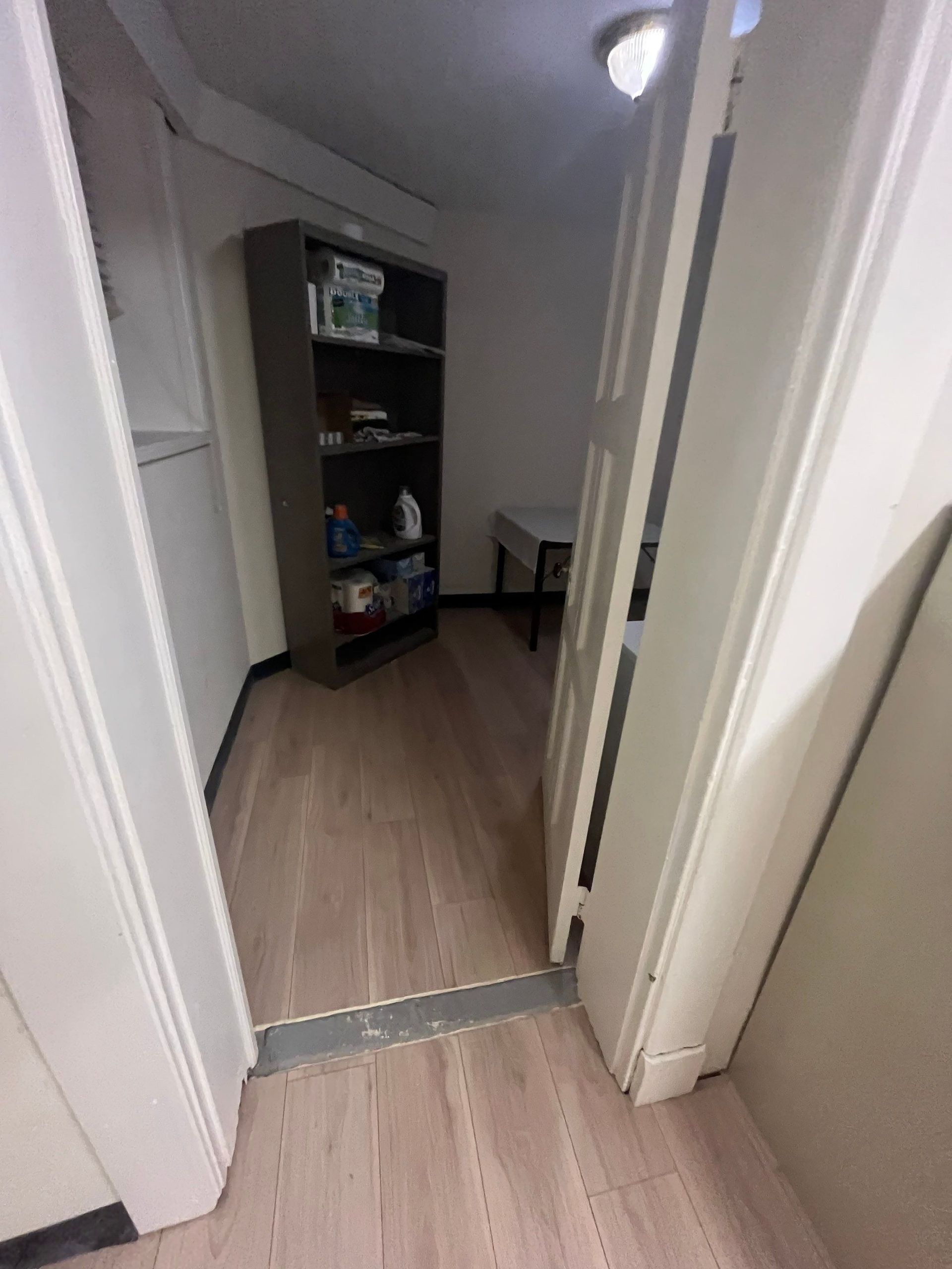 A narrow room with a bookshelf, white door, and wooden floor.