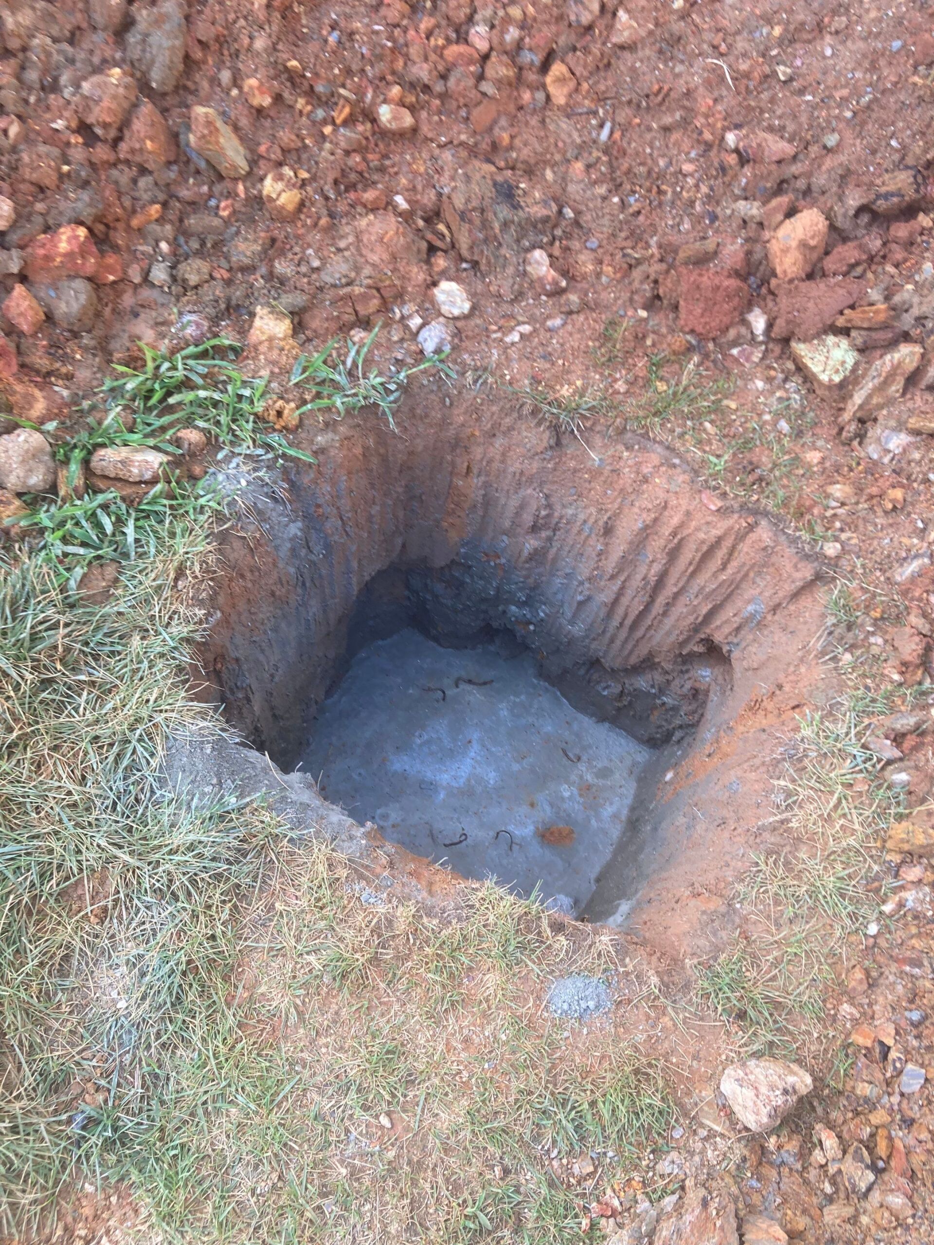 Hole dug in the ground with concrete base. Grass and dirt surround the opening.