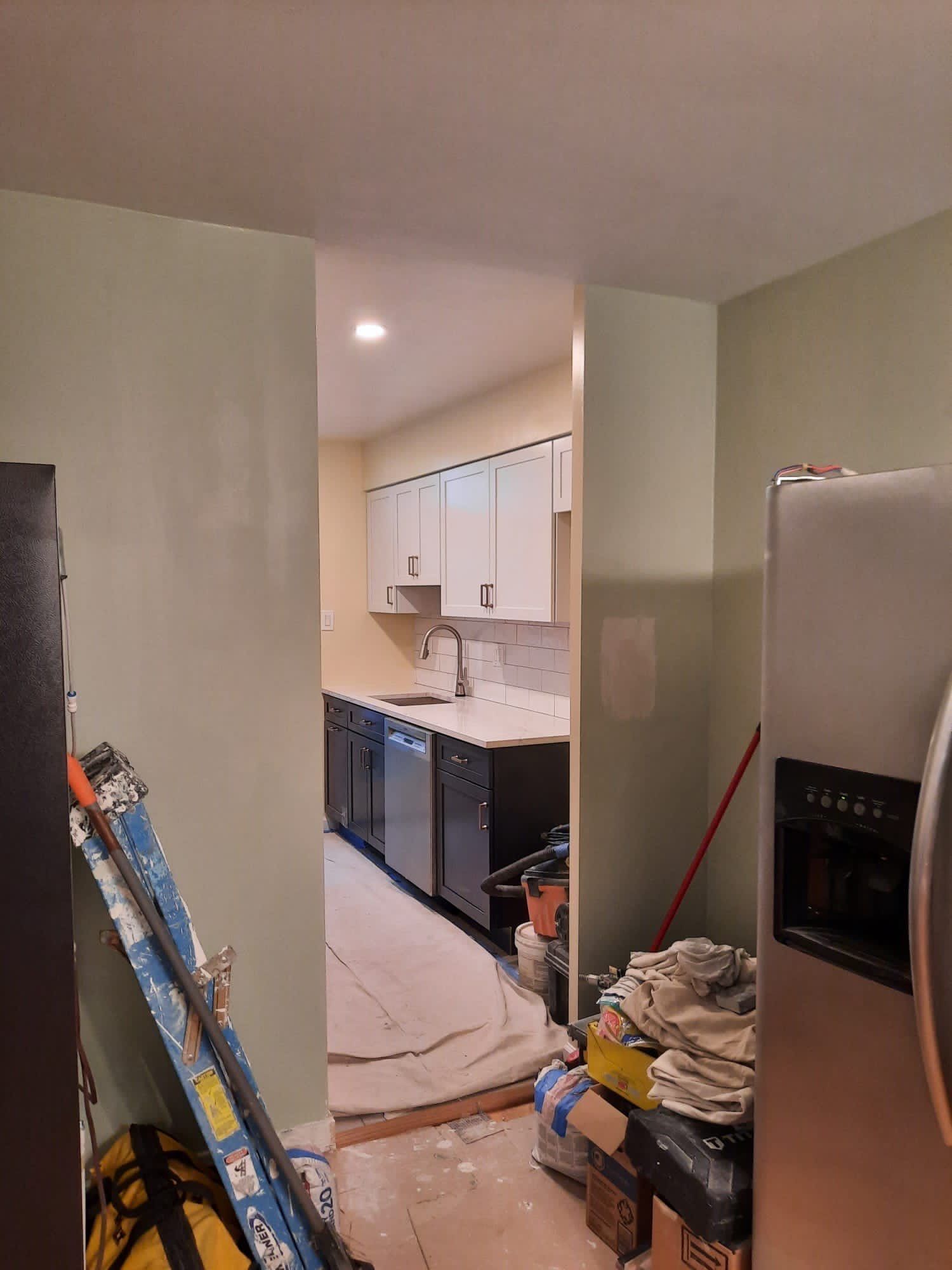 View into a kitchen: white cabinets, stainless steel appliances, open doorway, and tools.