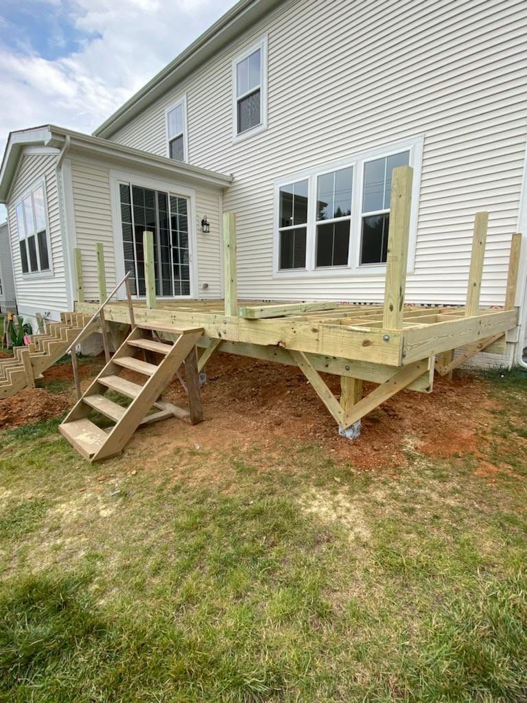 New wooden deck under construction; attached to a house with stairs and a railing.