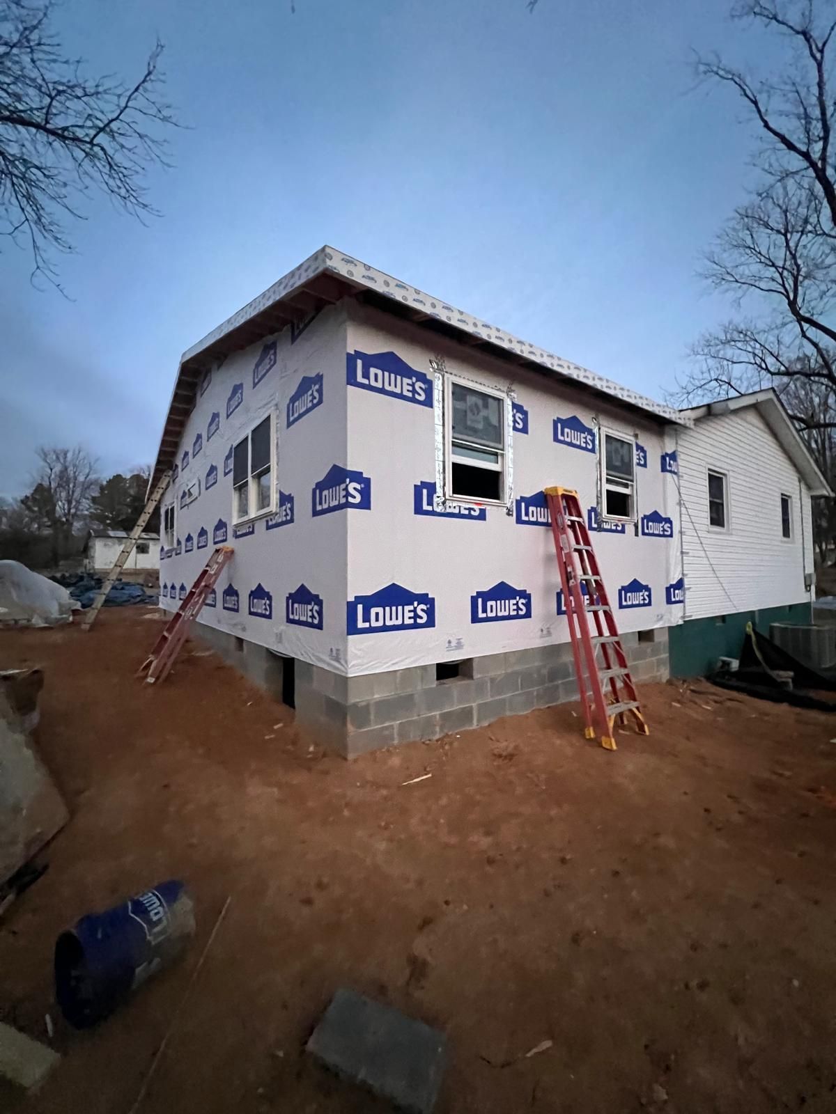 House under construction, covered in Lowe's branded wrap. Two ladders lean against the building.