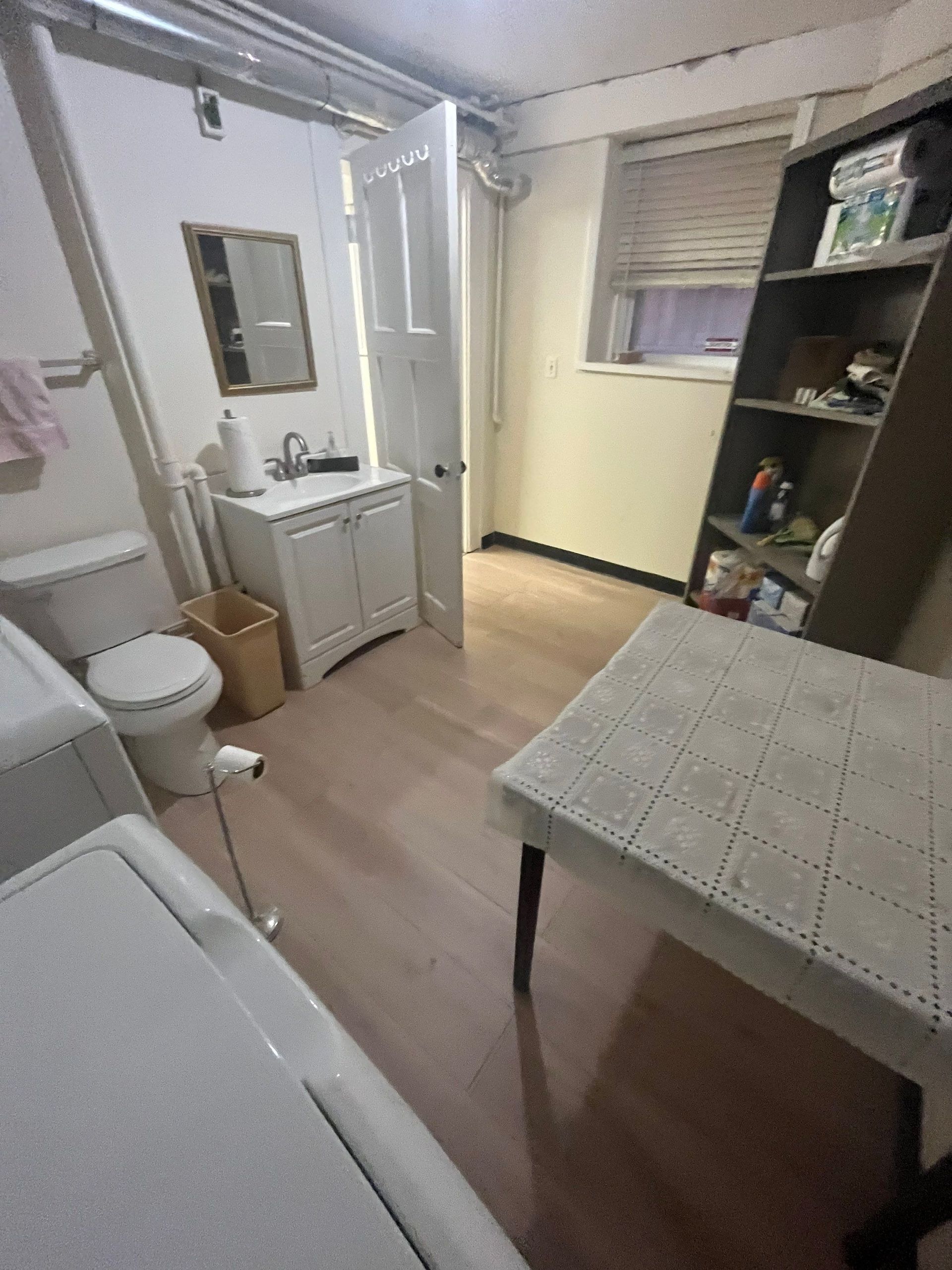 Bathroom with toilet, sink, washing machine, and table. Wooden floor and white door.