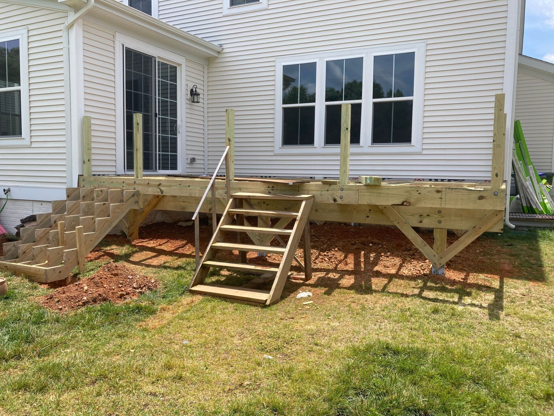 Newly constructed wooden deck with stairs leading to a house, set in a grassy yard.