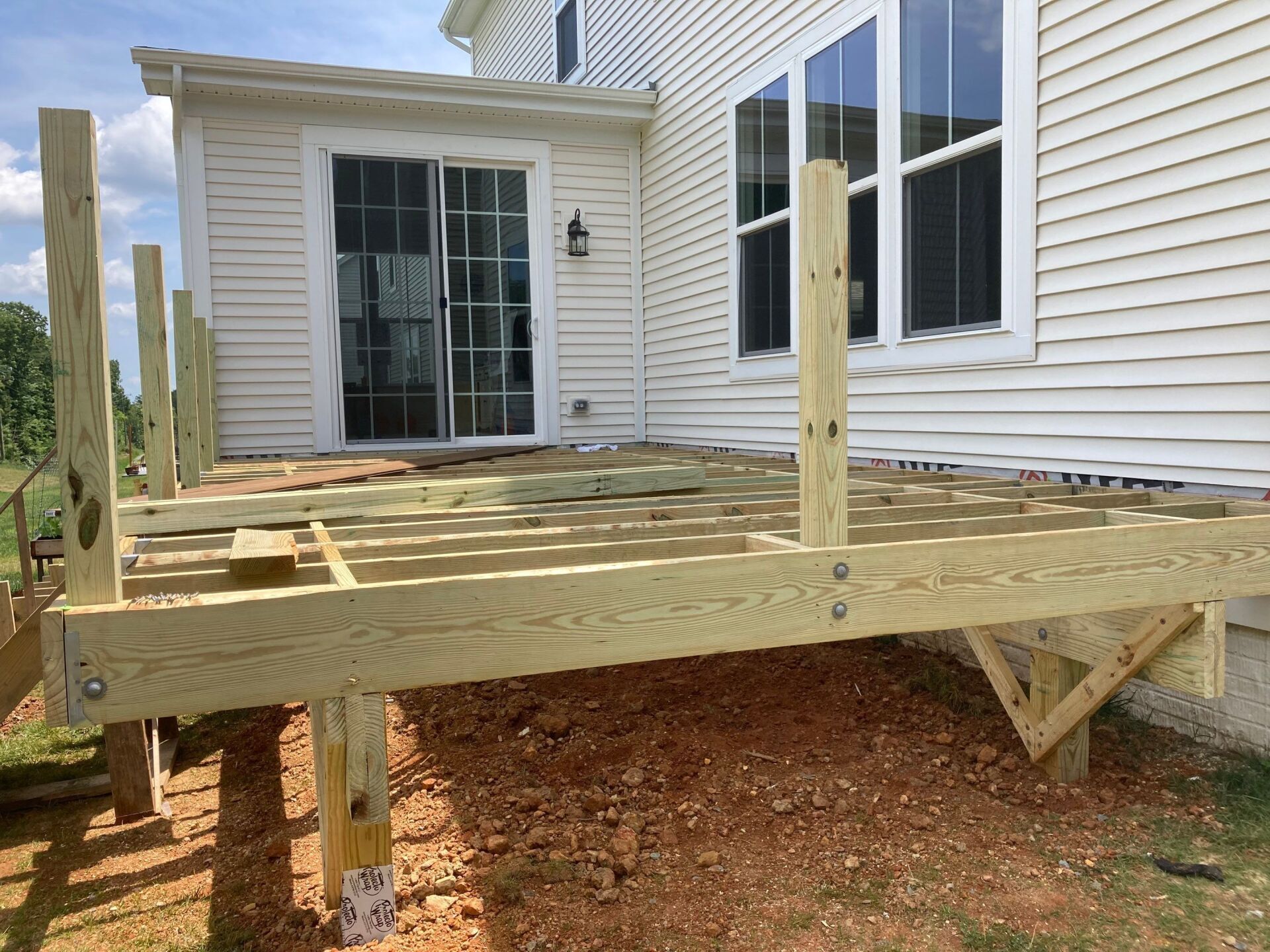 Wooden deck frame under construction near a white house with sliding glass door and windows.