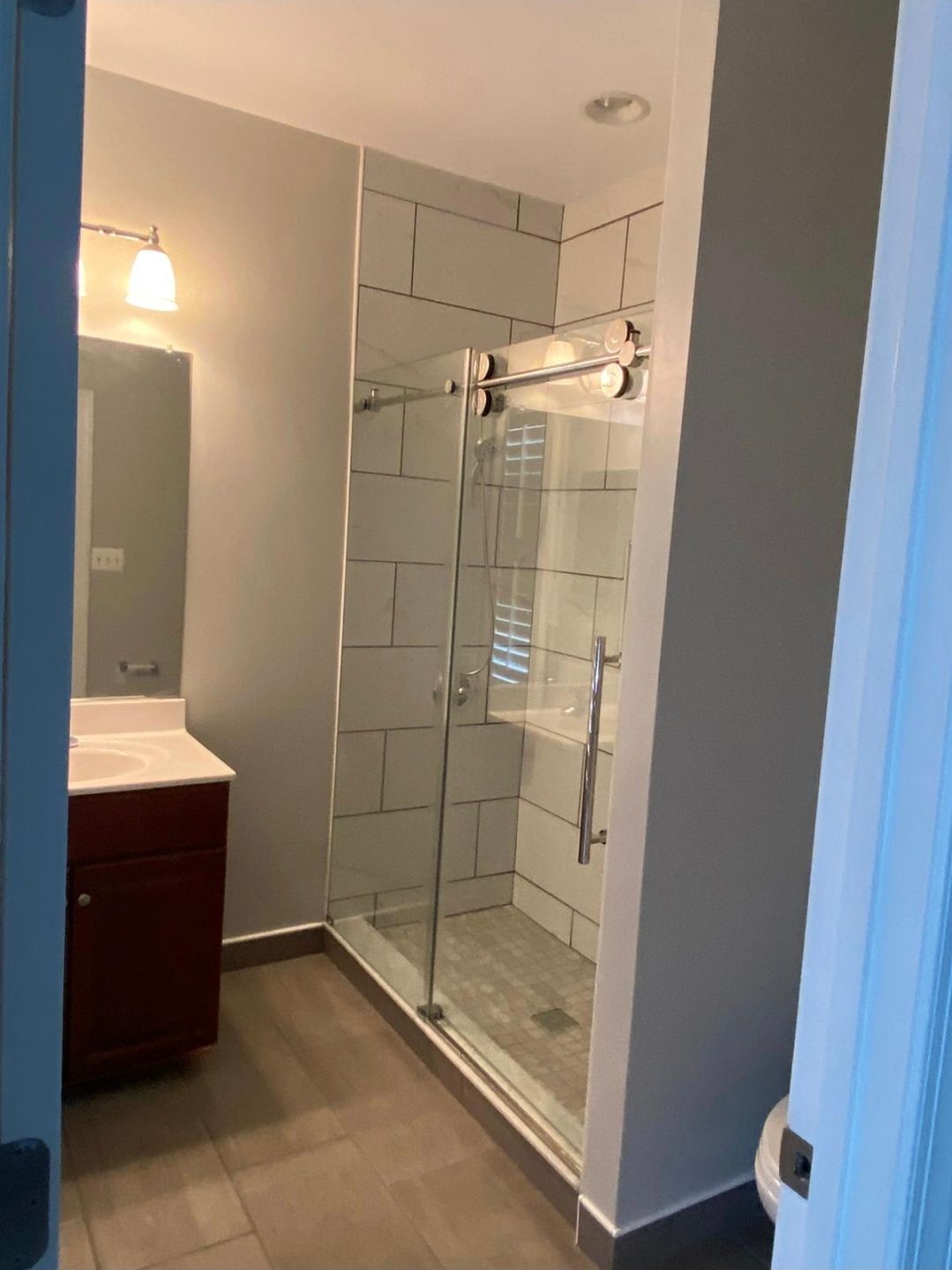 Bathroom with glass shower door, dark wood vanity, gray walls, and tile floor.