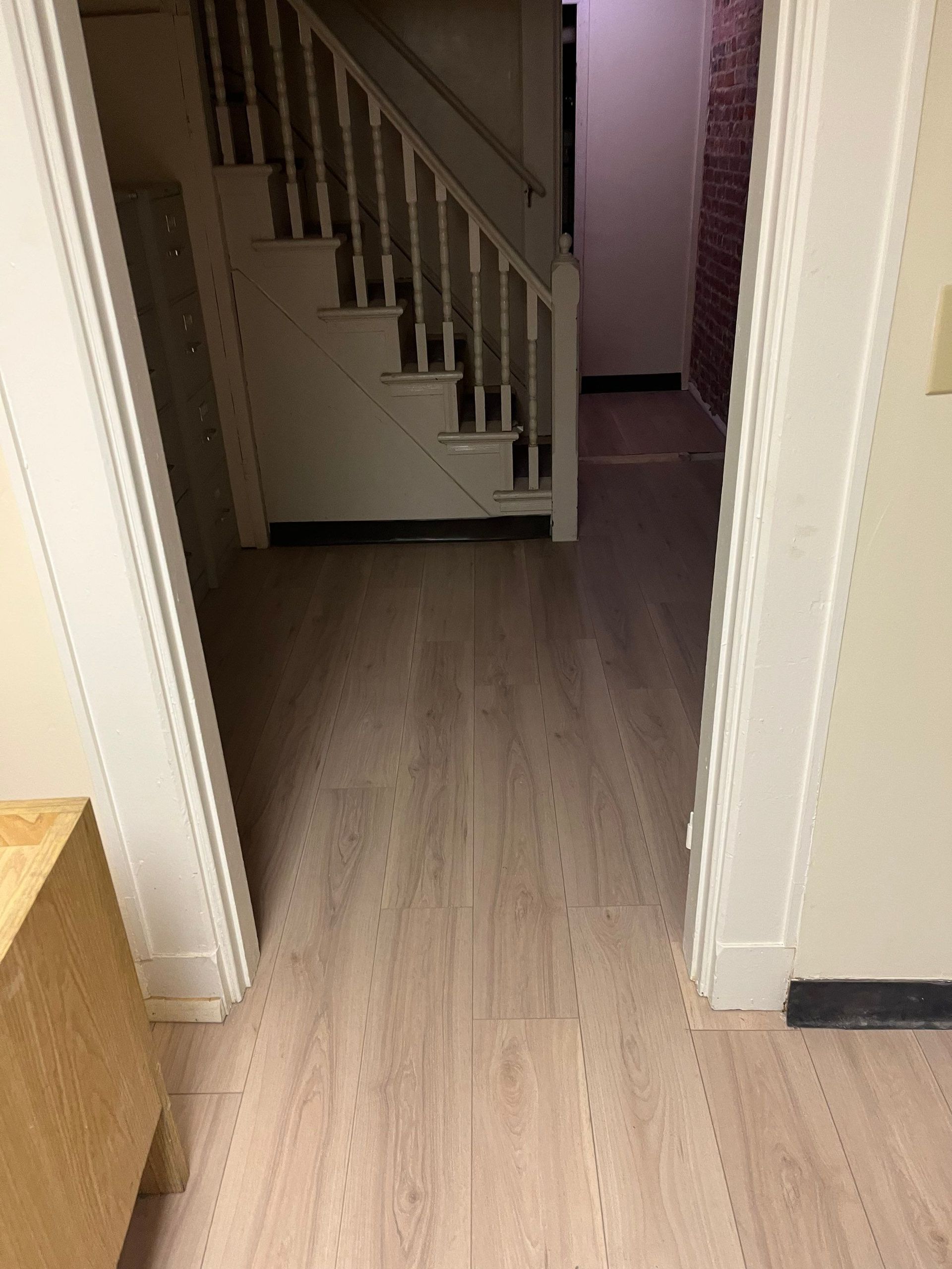 Hallway with light wood-look flooring, staircase, and doorway with white trim and beige walls.