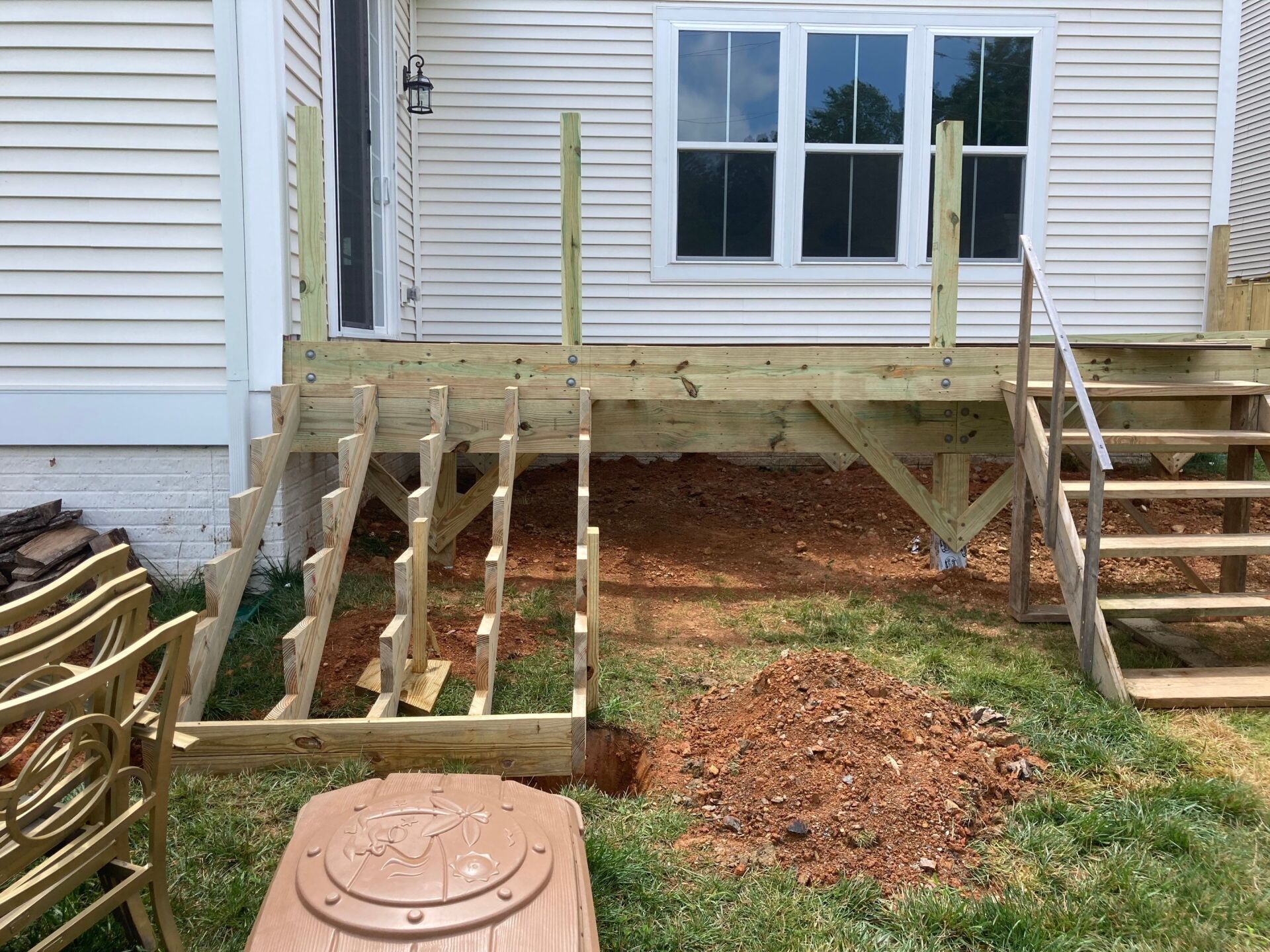 Partially constructed wooden deck and stairs next to a house, with exposed framing and dirt.