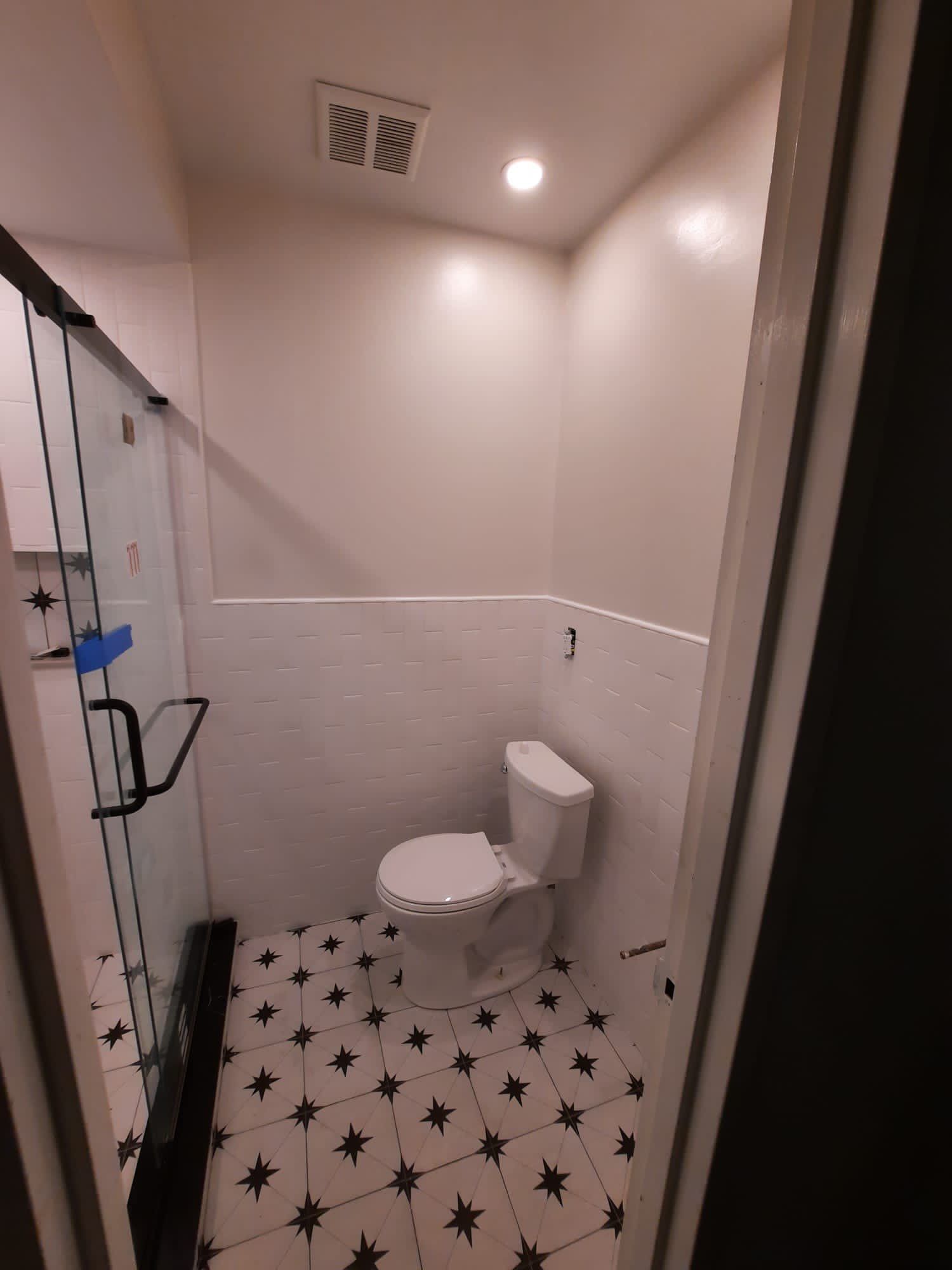 Small bathroom with white walls, patterned floor, toilet, and glass shower door.