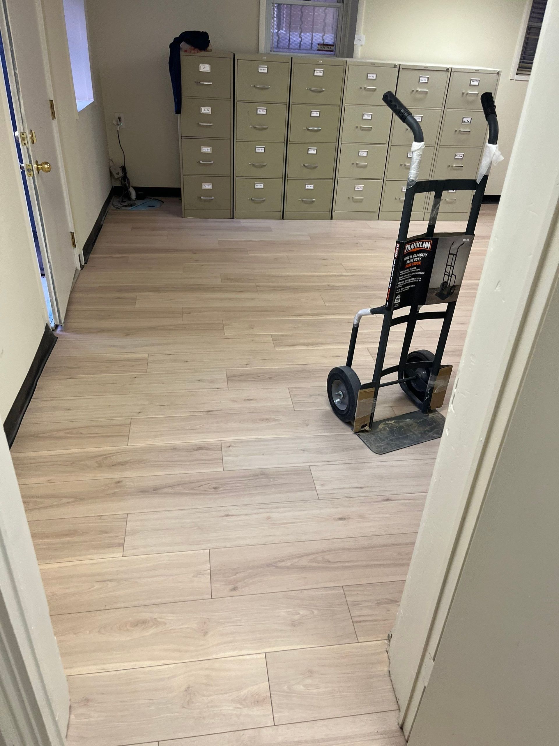 A room with light wood-look flooring, stacks of boxes, and a hand truck.