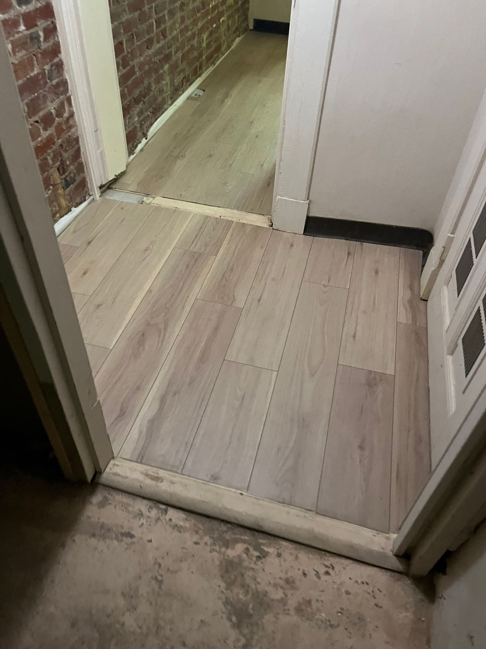 Light wood-look flooring installed in a doorway and hallway, transitioning from the entry.