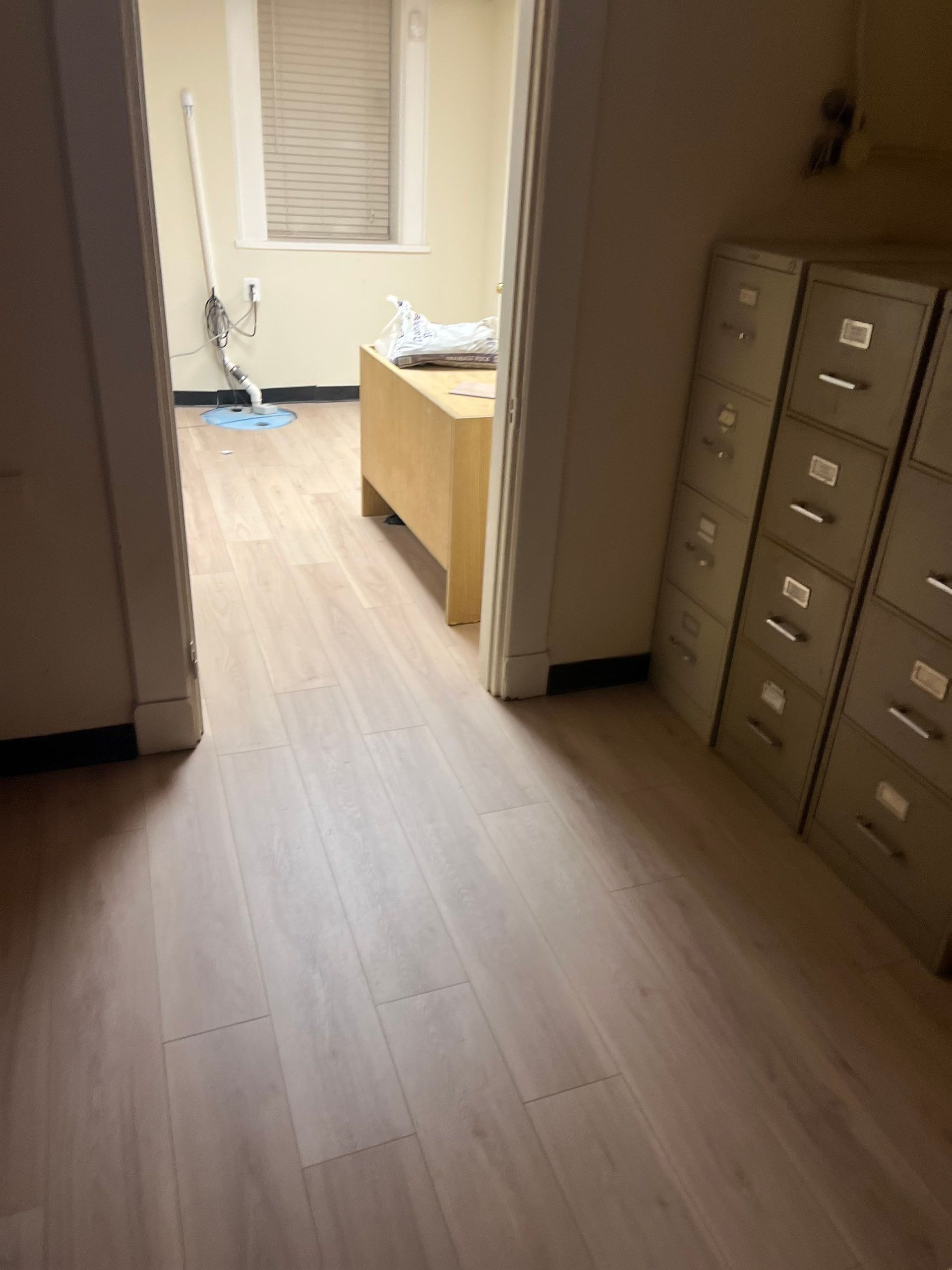 View from a doorway into an office space with light wood flooring, filing cabinets, and a desk.