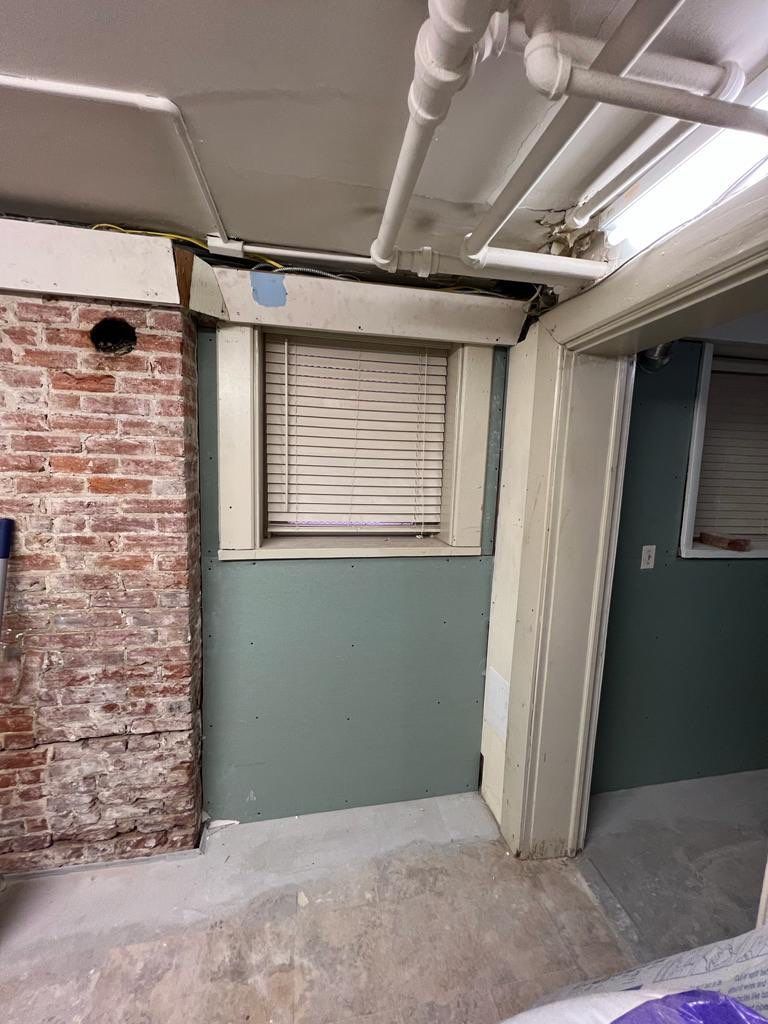 Basement interior with exposed brick chimney, window with blinds, and blue-green walls.