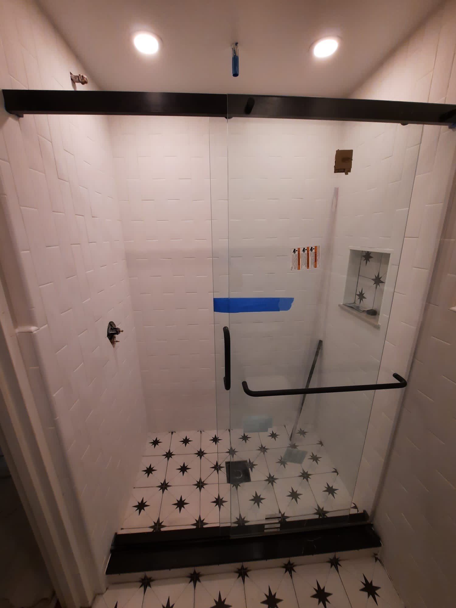 Modern shower with glass door and black fixtures. White subway tile walls, patterned floor.