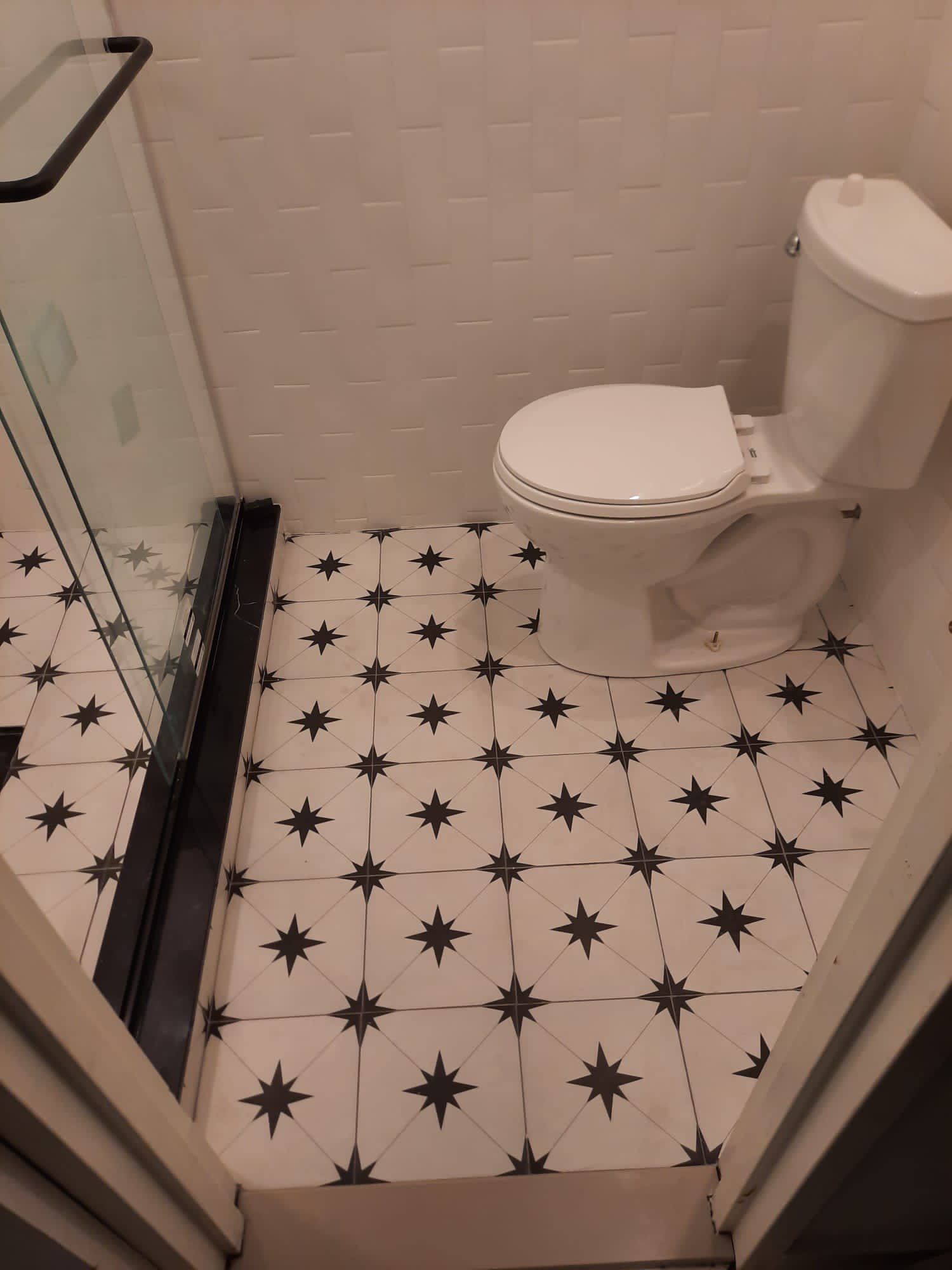Bathroom with star patterned floor tiles, white toilet, and glass shower door.