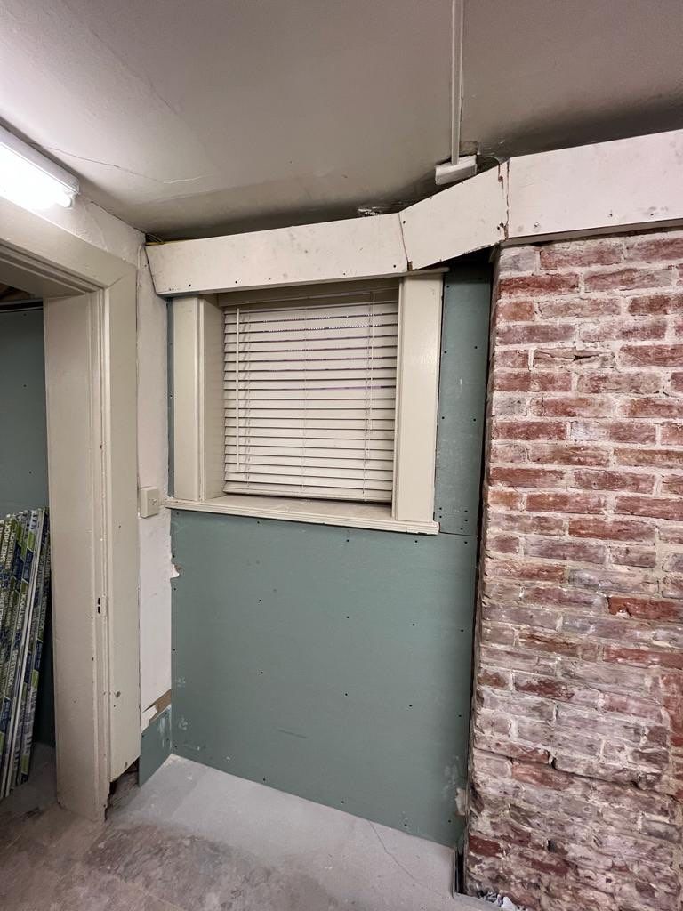 Window with blinds and brick wall in a room with light green walls and exposed ceiling.