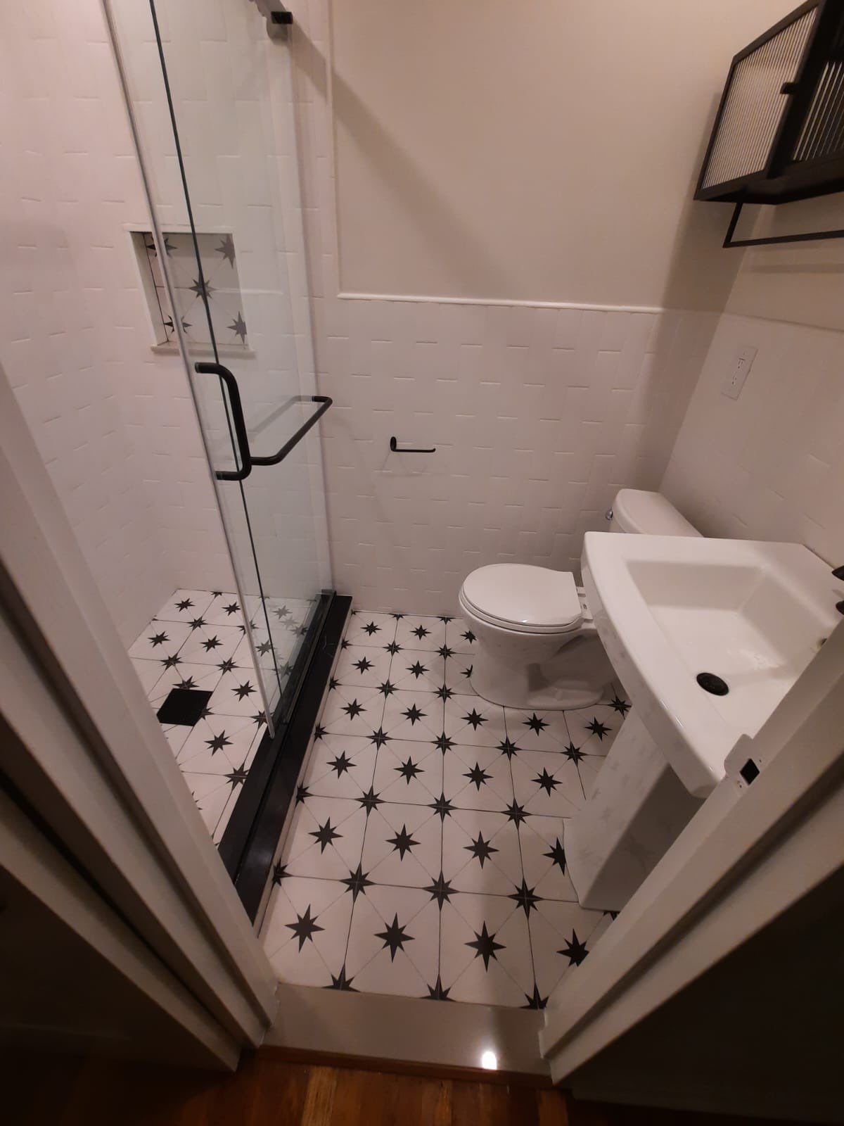 Small bathroom with black and white tile floor, white walls, and a glass shower.