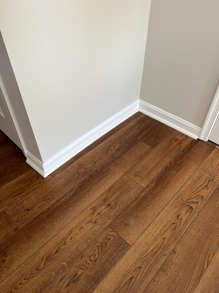 Corner of room with wood-look flooring, white baseboards, and light gray walls.