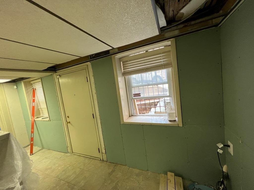 Interior view of a room under construction with green walls, a window, door, and a partially finished ceiling.