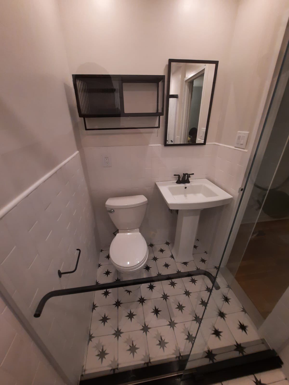 Small bathroom with white subway tile walls, pedestal sink, and star-patterned floor tiles.