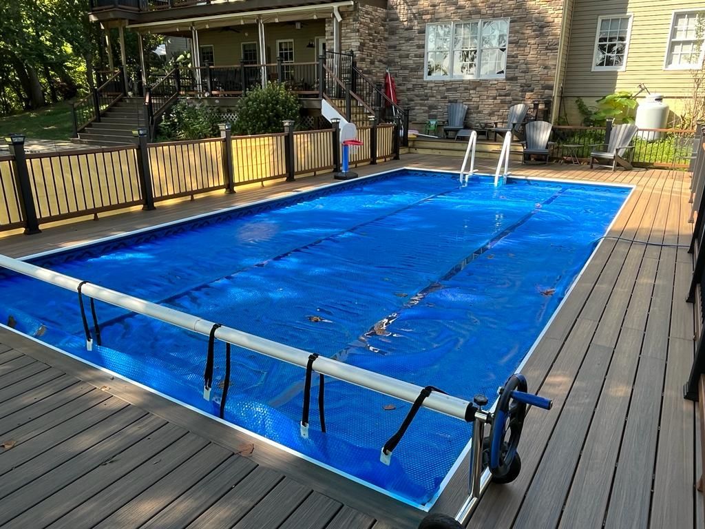 Blue pool cover on a rectangular pool in a backyard, surrounded by a deck and a fence.