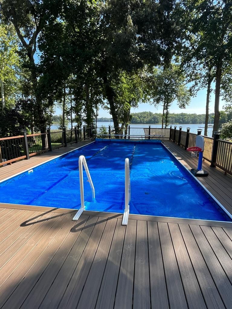 Rectangular pool covered with blue tarp on a wooden deck overlooking a lake.