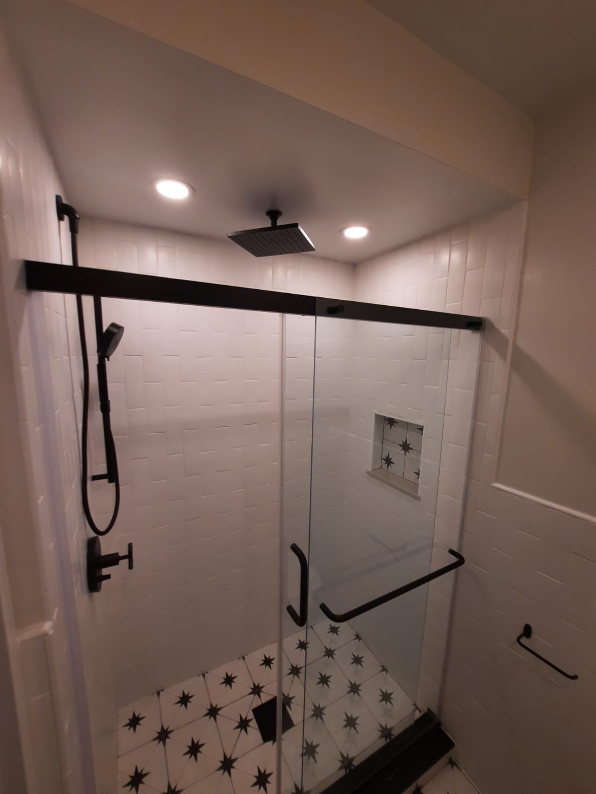 Modern shower with black fixtures, glass door, and white and patterned tile.