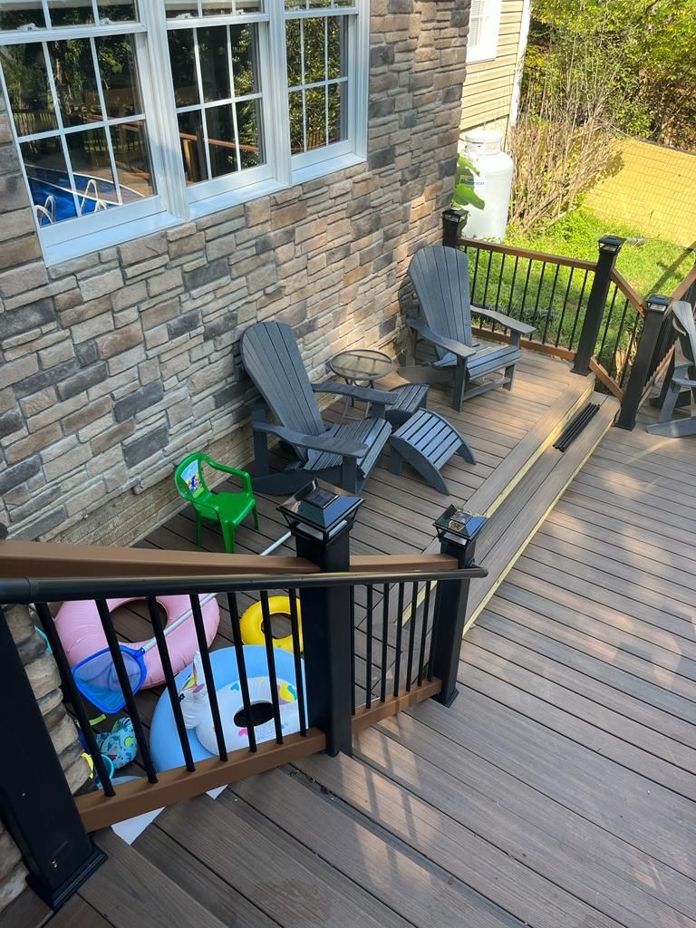 Outdoor deck with two Adirondack chairs, railing, and a stone facade house.