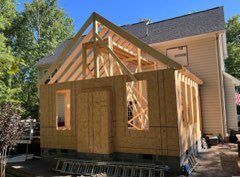 House addition under construction; wooden framing, siding, and roof structure visible.