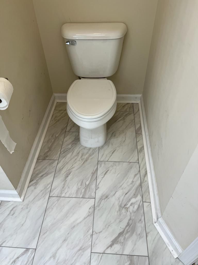 Toilet in a small bathroom with gray and white tiled floor and beige walls.