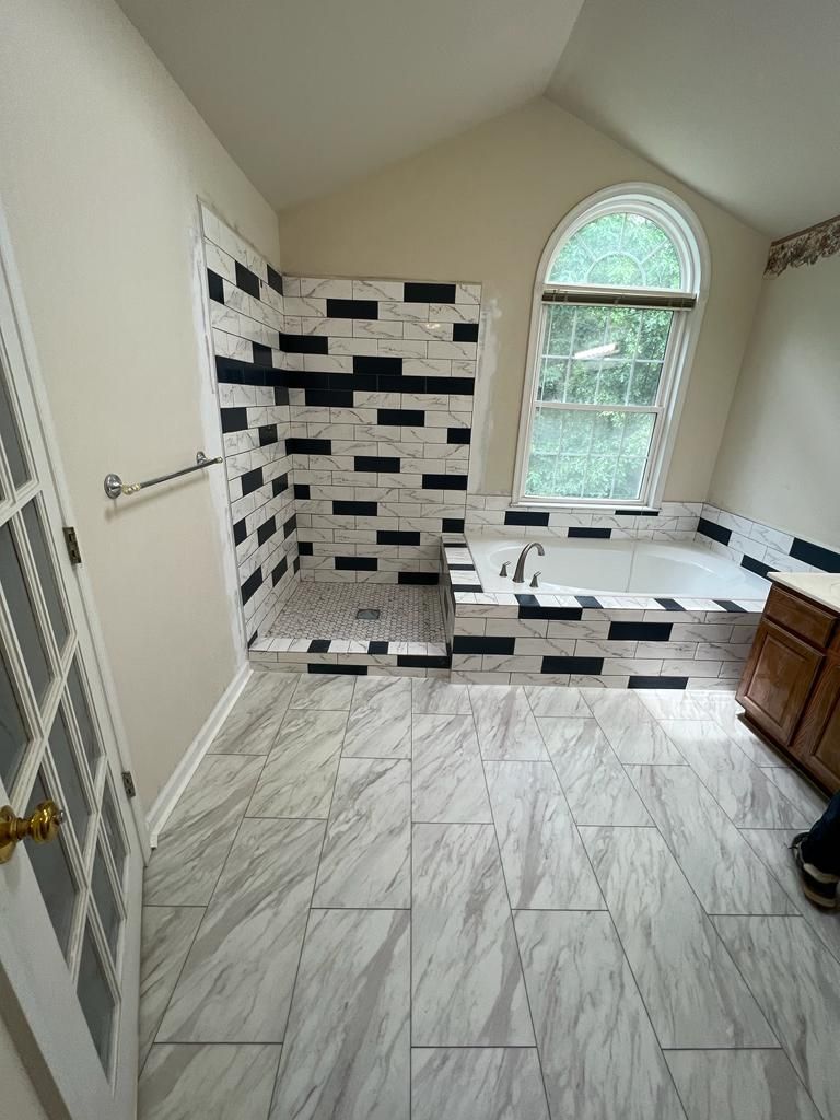 Bathroom with new tiling: white and gray floor, black and white shower wall, bathtub near arched window.