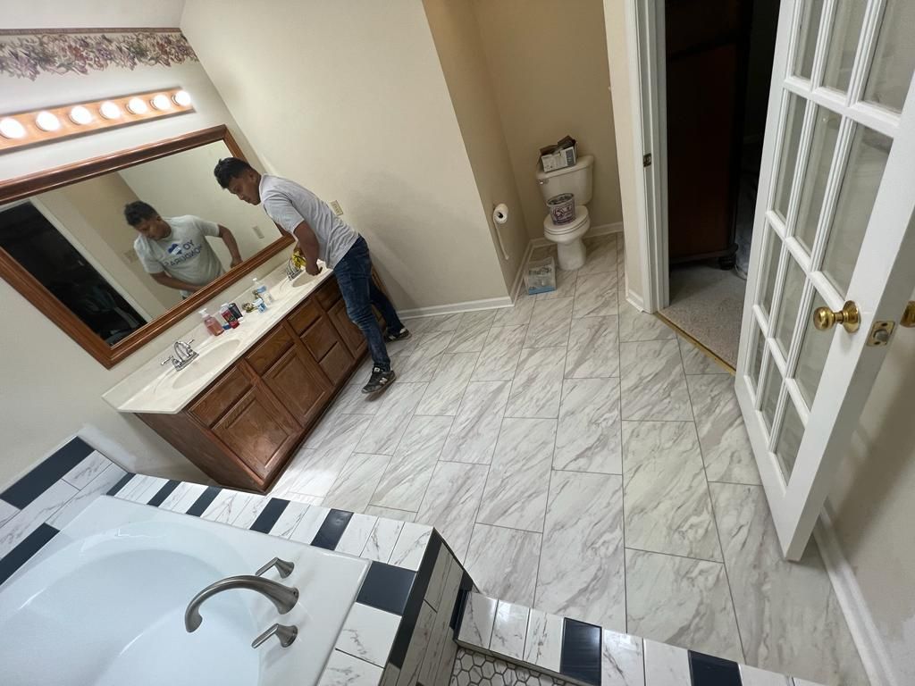 Person cleaning bathroom with white tile floor, tub, vanity, and toilet.
