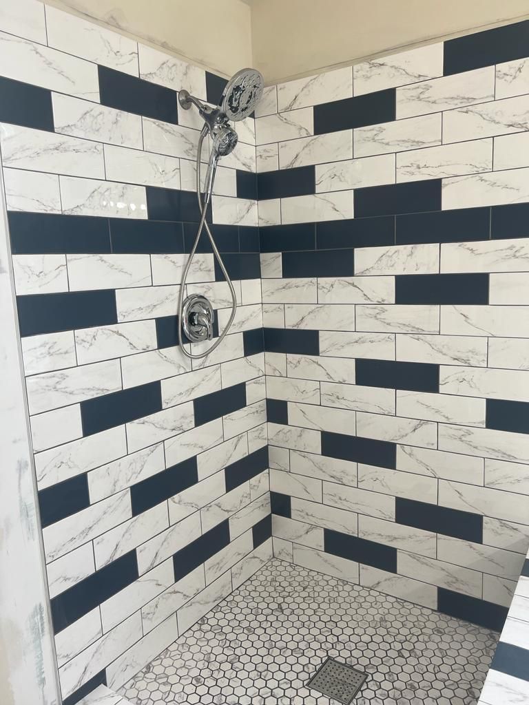 Shower with white marble-look tiles and navy horizontal stripes. Silver showerhead and fixtures.