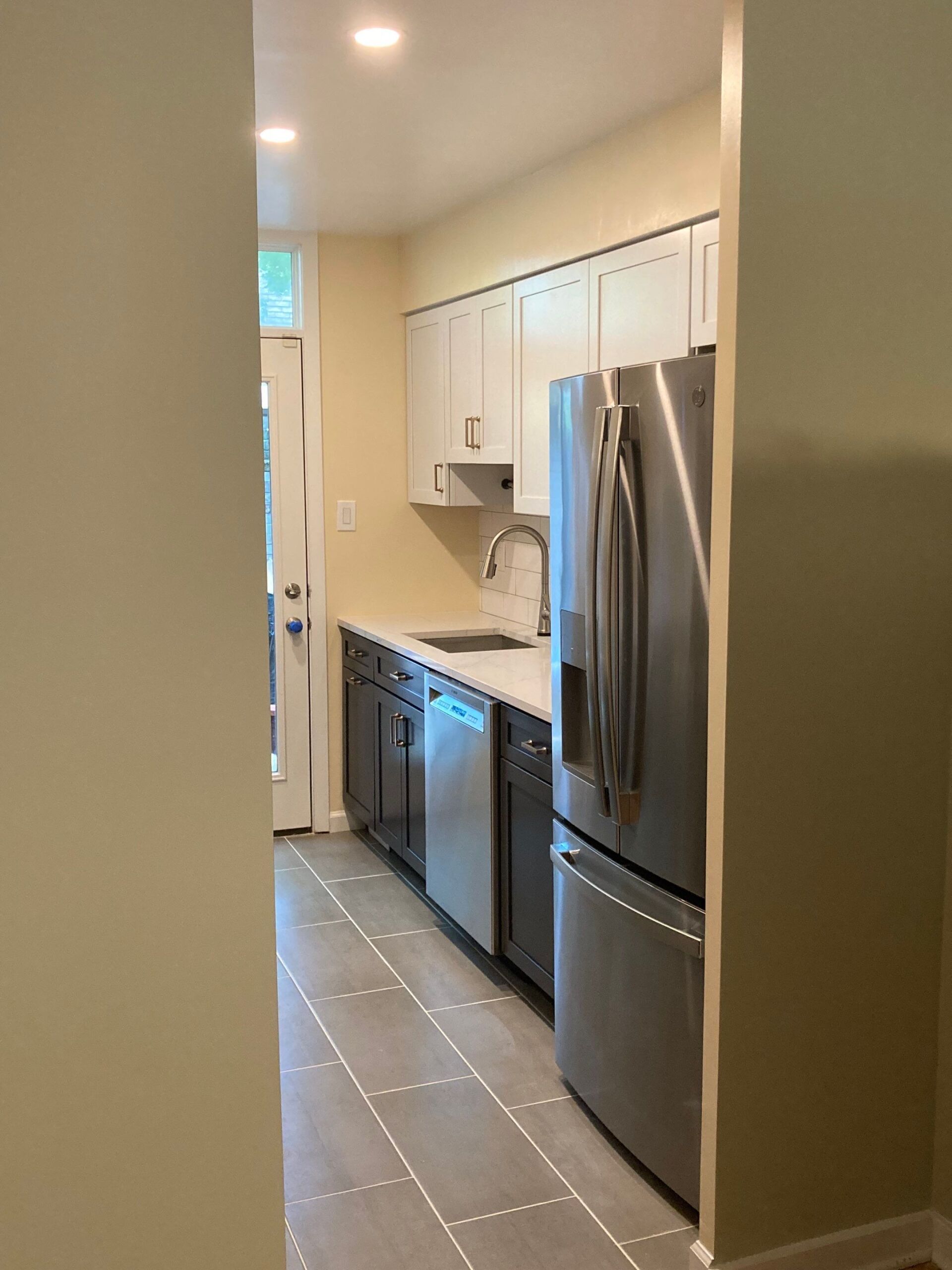 Narrow kitchen with stainless steel appliances, white cabinets, and light gray flooring.